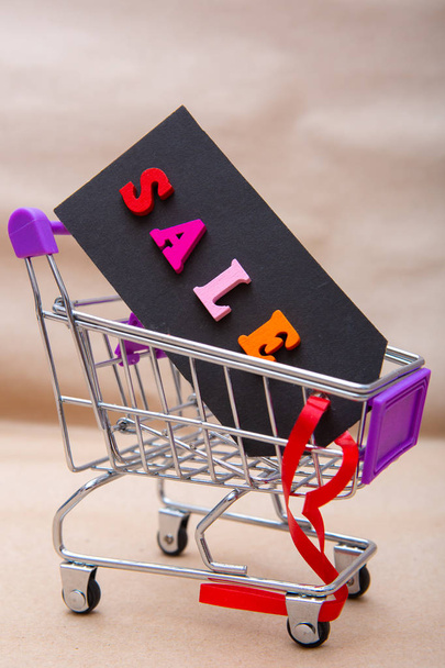 black tag with the words sale in Caddy for shopping. Cardboard label with the inscription sale on the background of Kraft paper. Holiday sales concept - 写真・画像