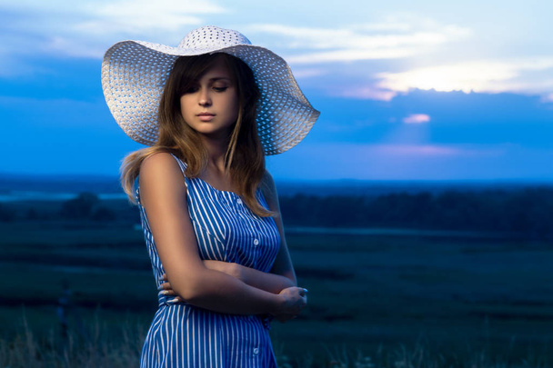 dramatic portrait of a beautiful girl in a hat in the field, a young woman is walking in the summer outdoors - Photo, image