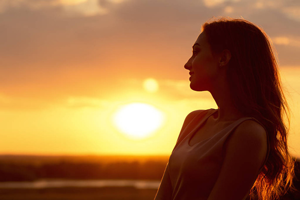 silhouette of a beautiful girl at sunset in a field, face profile of young woman enjoying nature - Φωτογραφία, εικόνα