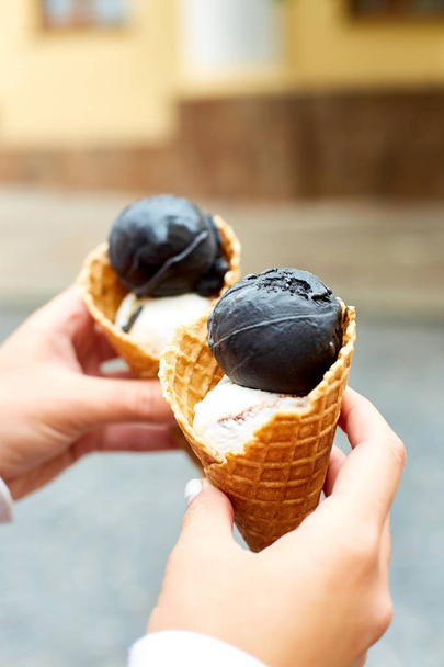 女性の手保有物 2 つ炭と都市背景のワッフル コーンにアイスクリームします。イタリアの伝統的なアイス クリーム ジェラート。コピー スペース. - 写真・画像