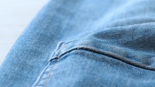 Crumpled blue jeans laying on the desk, close shot close shot. Macro dolly shot. Selective soft focus. Camera moving along seams and rear trouser pocket - Video