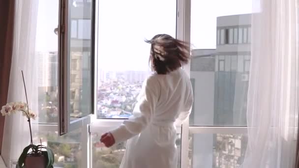 Attractive brunette woman in white bathrobe enjoying her new apartments for vacation. Happy Girl Dancing and falling on sofa. - Séquence, vidéo