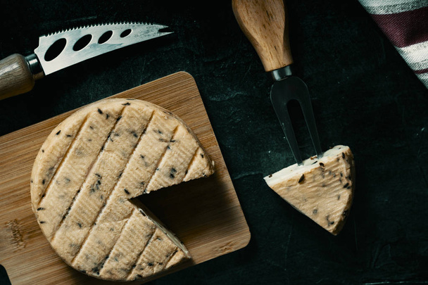 Overhead Bild von Käse mit Gewürzen auf Holzbrett und spezielle Messer und Gabel für den Käse auf der Seite - Foto, Bild