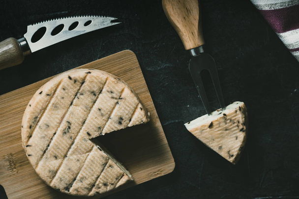 Εναέρια εικόνα του τυριού με μπαχαρικά σε ξύλινη σανίδα και ειδικό μαχαίρι και πιρούνι για το τυρί στο πλάι - Φωτογραφία, εικόνα