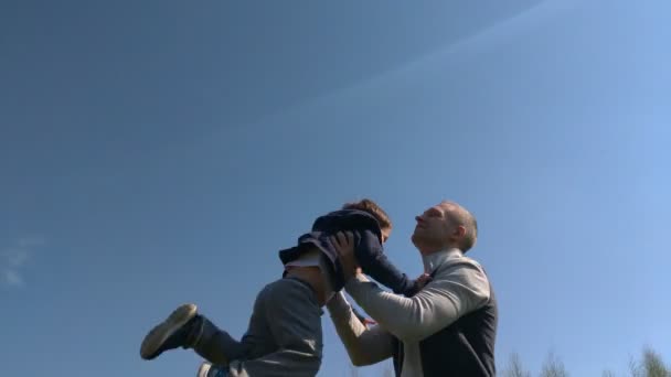 Táta hází syna vysoko do výšky, dítě letní slunného dne. Zpomaleně. otec a syn se baví venku - Záběry, video