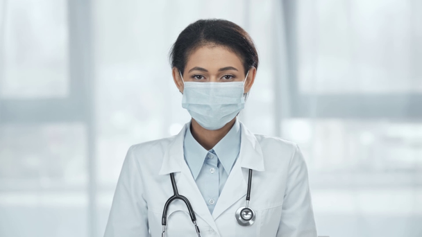 Africano americano médico em casaco branco com estetoscópio em máscara médica olhando para a câmera
 - Filmagem, Vídeo