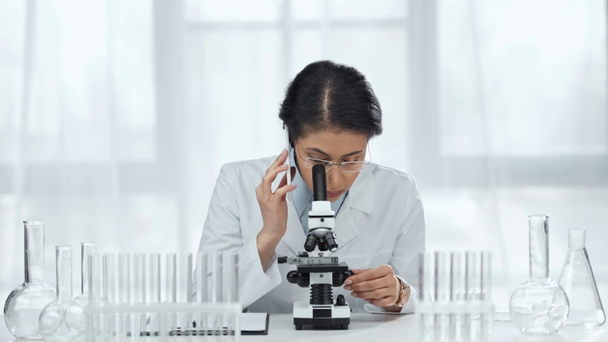 un scientifique afro-américain parlant sur smartphone et regardant un échantillon au microscope en laboratoire
  - Séquence, vidéo