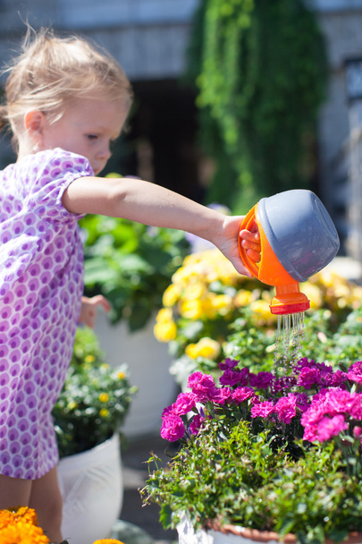Маленька мила дівчинка поливає квіти з лійкою
 - Фото, зображення