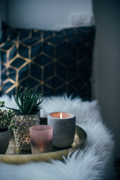 Затишна справжня домашня прикраса, палаючі свічки на золотому підносі з подушкою на білому штучному хутрі на підвіконні
 - Фото, зображення
