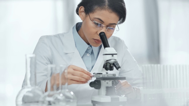 szelektív középpontjában az afroamerikai tudós szemüveg nézi minta mikroszkóppal laboratóriumi  - Felvétel, videó