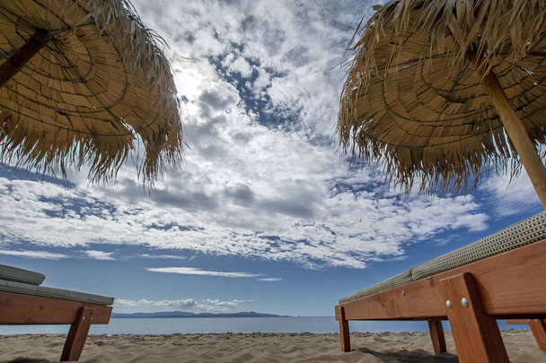 Gyönyörű kis szög jelenet szalma napernyőkkel, fából készült napozóágyak, homokos tengerpart és a kék tenger a felhős ég. Természetes keret, tökéletes hátteret design és szöveg. Vakáció és utazási koncepció - Fotó, kép