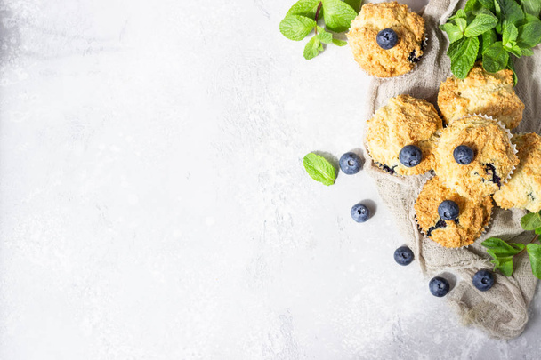 Blueberry muffins with fresh berries and mint leaves on light grey stone background. Copy space. - Foto, Imagen
