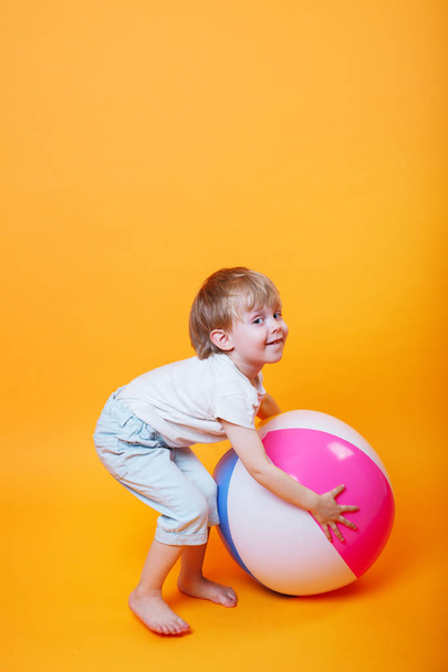 Cute Llttle boy in swimming shorts holding a beach ball on orange background - Foto, Imagem