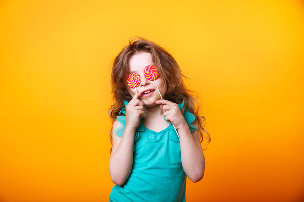 Portrait of cute little girl with candy on a yellow background. - Photo, image