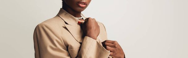bijgesneden weergave van trendy Afro-Amerikaanse vrouw in beige jasje geïsoleerd op grijs - Foto, afbeelding