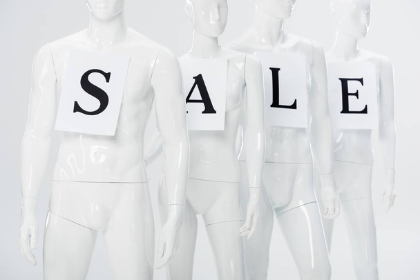 papers with sale lettering on white plastic mannequins isolated on grey - Foto, Bild