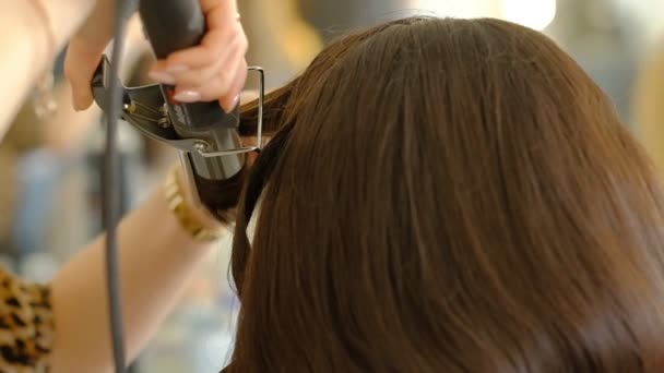 女性の美容師は、髪のアイロンを使用して、髪を圧着し、クライアントにボリュームのあるヘアスタイルを行います。職場でプロの美容師。スローモーション - 映像、動画