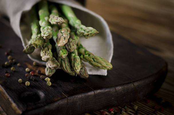 Green juicy asparagus is lying on a wooden board on a brown wooden table. - 写真・画像