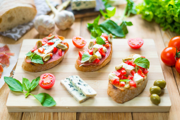 Toasted ciabatta, a cheese sandwich with mold, tomatoes, basil on a wooden background. - Foto, afbeelding