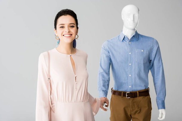 beautiful smiling girl holding hands with mannequin isolated on grey - Photo, Image