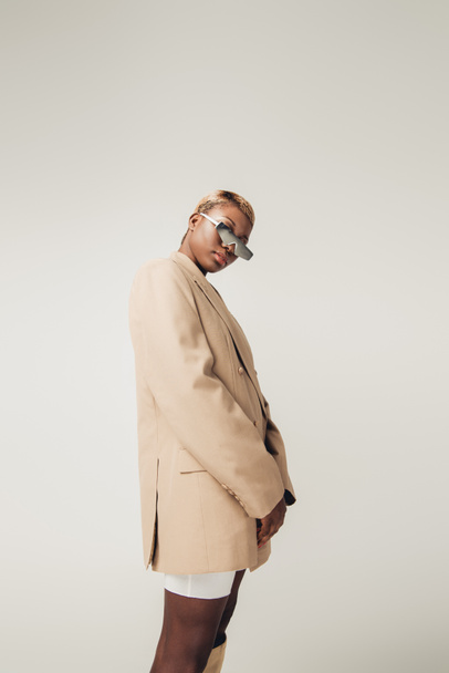 african american girl posing in sunglasses and beige jacket isolated on grey - Foto, immagini
