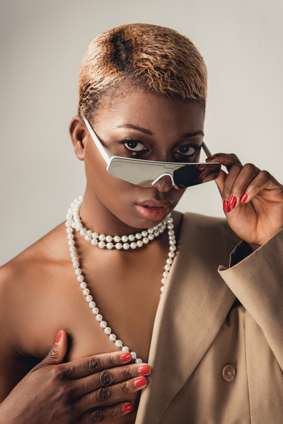 naked african american girl posing in sunglasses and beige jacket isolated on grey - Фото, зображення