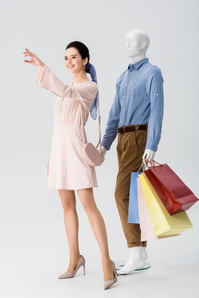 beautiful girl gesturing near mannequin with shopping bags on grey - Photo, Image