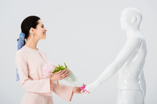 beautiful girl taking flower bouquet from mannequin isolated on grey - Photo, Image