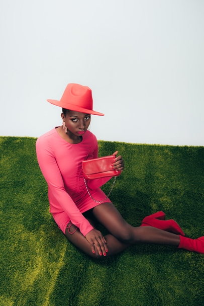 красивая африканская американка в розовом платье и шляпе позирует с мешком на зеленой траве
 - Фото, изображение