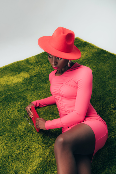 young african american model in pink dress and hat posing with bag on green grass - Fotoğraf, Görsel