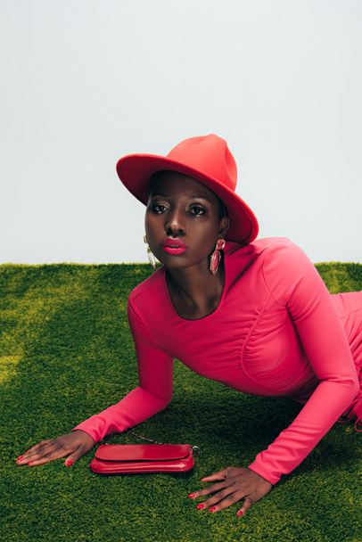 glamorous african american girl in pink dress and hat posing with bag on green grass - 写真・画像