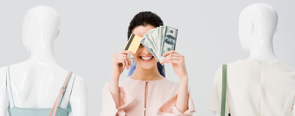 plano panorámico de chica cerca de maniquíes cubriendo la cara con dinero y tarjeta de crédito aislado en gris
 - Foto, imagen