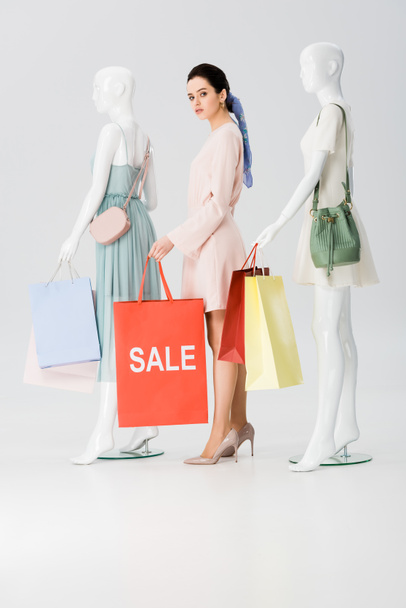 hermosa mujer joven con palabra venta en bolsa de compras cerca de maniquíes en gris
 - Foto, imagen
