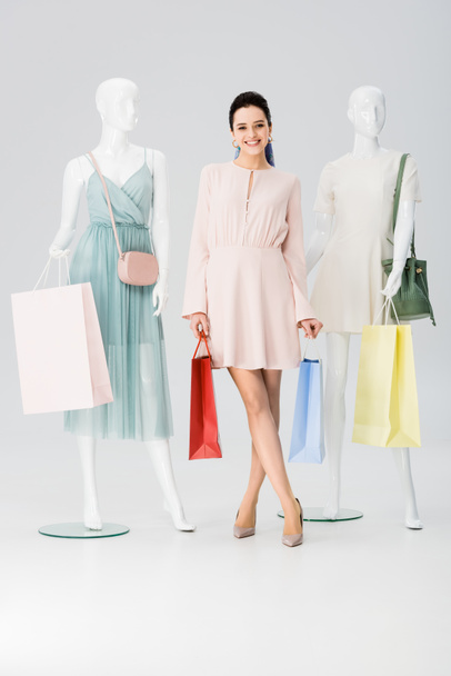 beautiful smiling young woman with shopping bags near mannequins on grey - Foto, imagen