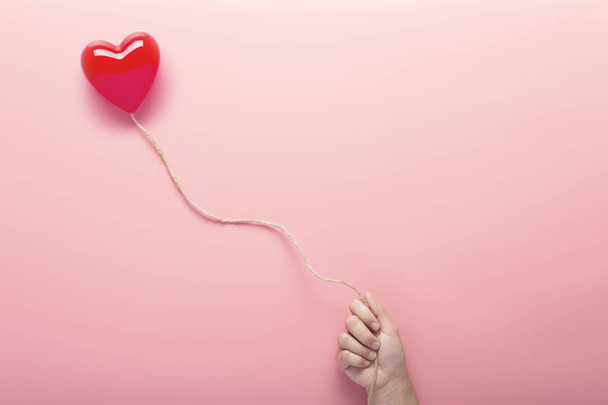 Χέρι κρατώντας κόκκινο του Αγίου Βαλεντίνου πλαστικό μοντέλο καρδιάς σε σχοινί επιπλέει  - Φωτογραφία, εικόνα