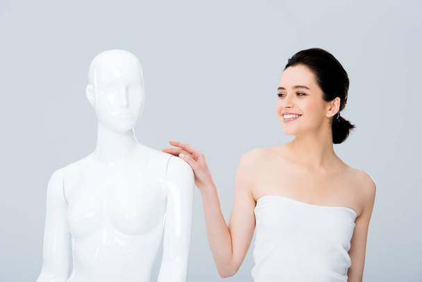 atrakcyjne uśmiechnięta młoda kobieta w białym pozowanie z manekina na białym tle na szary - Zdjęcie, obraz