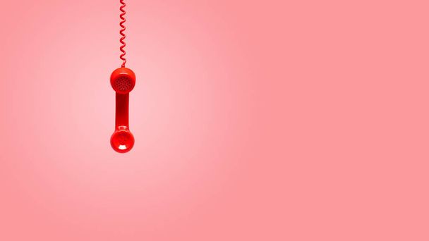 Red old telephone receiver hanging on pink background - Foto, Imagen
