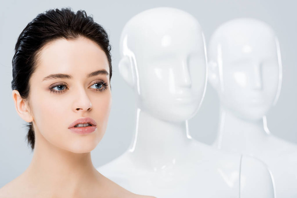 beautiful girl posing in row with white mannequins isolated on grey - Photo, image