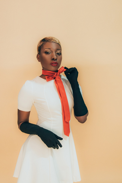 stylish african american girl posing in trendy red scarf and black gloves isolated on beige - Photo, Image