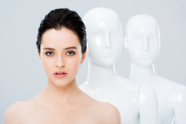 beautiful nude girl posing in row with white mannequins isolated on grey - Фото, зображення
