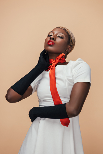 sexy african american girl posing in white dress, red scarf and black gloves isolated on beige - Foto, afbeelding