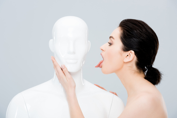 mooie jonge vrouw steekt tong in de buurt mannequin geïsoleerd op grijs - Foto, afbeelding
