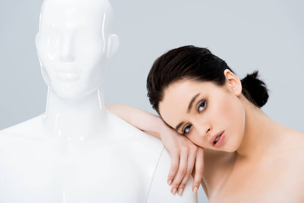 beautiful young woman leaning on mannequin and looking at camera isolated on grey - Photo, Image