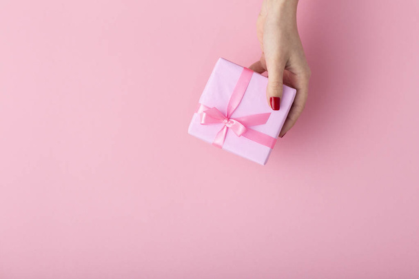 girl holding a present in hands, women's hands open the box wrapped in decorative paper on a pastel pink background, top view, concept holiday and gifts - Zdjęcie, obraz
