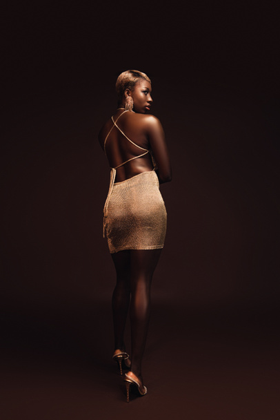 hermosa mujer afroamericana elegante con el pelo corto posando en vestido glamoroso en marrón
 - Foto, imagen