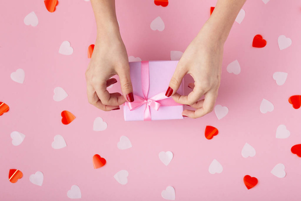 female hands with a gift box on a pastel colored background top view, the girl opening a present and untying a ribbon bow, the concept of holidays - Foto, Imagem