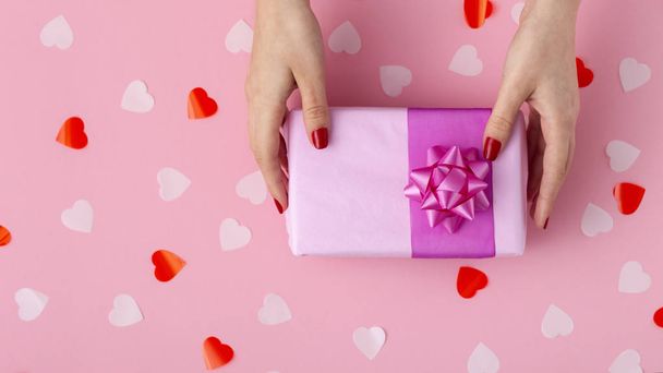 female hands with a gift box on a pastel colored background top view, the girl holding a present with decorations, the concept of holidays and love - Photo, Image
