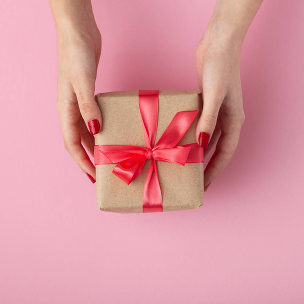 手にプレゼントを持っている女の子、ピンクの背景、トップビュー、コンセプトホリデーや贈り物に装飾紙に包まれた手にギフトボックスを持つ女性 - 写真・画像