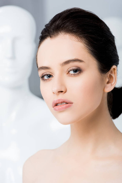 beautiful girl posing near mannequin and looking at camera isolated on grey  - Фото, изображение