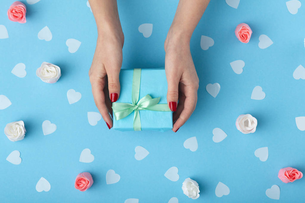 female hands with a gift box on a pastel colored background top view, the girl holding a present with decorations, the concept of holidays and love - 写真・画像